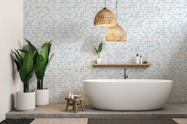 May include: A white bathtub with a black faucet sits in a bathroom with light blue mosaic tile walls. Two woven pendant lights hang from the ceiling. Two potted plants are on the left side of the image. A small wooden stool with a white towel sits in front of the bathtub.