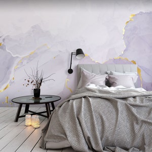 May include: A bedroom with a bed with a gray duvet and white pillows. The wall behind the bed is painted with a light purple and gold abstract design.