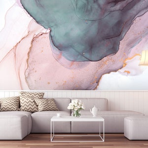 May include: A white sectional sofa with brown patterned throw pillows sits in front of a wall with an abstract painting featuring pink, teal, and gold swirls. A white coffee table sits in front of the sofa with a white teapot and a bouquet of white flowers.