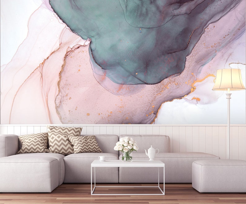 May include: A white sectional sofa with brown patterned throw pillows sits in front of a wall with an abstract painting featuring pink, teal, and gold swirls. A white coffee table sits in front of the sofa with a white teapot and a bouquet of white flowers.