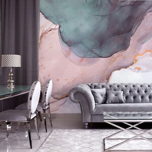 May include: A living room interior featuring a grey tufted sofa, two grey chairs, a glass-topped coffee table, and a lamp with a patterned shade. The wall behind the furniture is adorned with a large abstract painting in shades of pink, green, and gold.