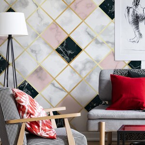 May include: A modern living room with a geometric wallpaper featuring marble-like patterns in white, pink, and dark green, accented by gold lines. A patterned armchair and a gray sofa with red pillows complement the design.