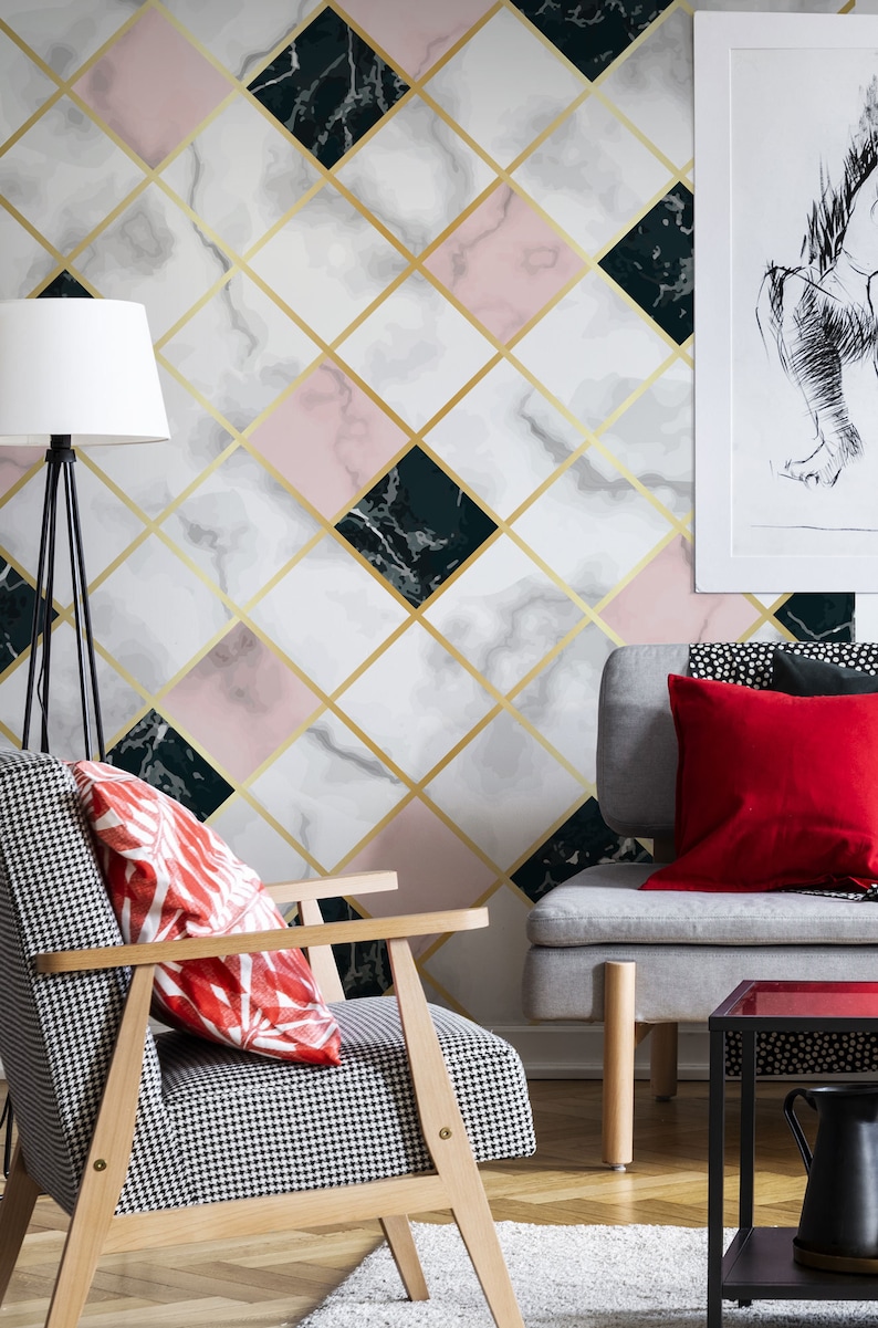May include: A modern living room with a geometric wallpaper featuring marble-like patterns in white, pink, and dark green, accented by gold lines. A patterned armchair and a gray sofa with red pillows complement the design.