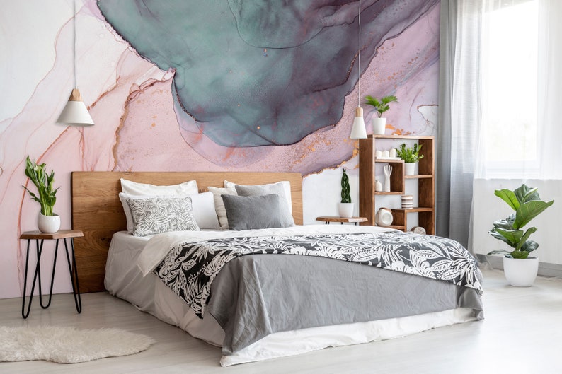 May include: A bedroom with a grey and white patterned bedspread, a wooden headboard, and a pink and blue abstract wall mural. There are two bedside tables with plants and lamps.