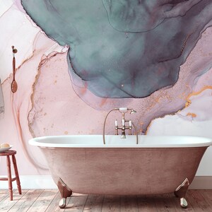 May include: A freestanding bath with a gold tap in a bathroom with a pink, white and teal abstract watercolour wallpaper.