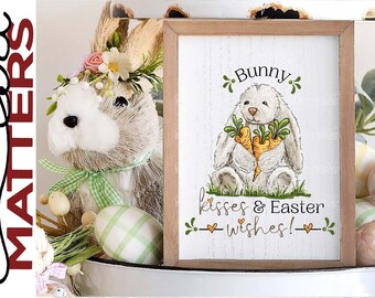 May include: A white wooden sign with a brown frame features a cartoon bunny holding carrots. The sign reads "Bunny kisses & Easter wishes!" with green leaves and hearts around the text.