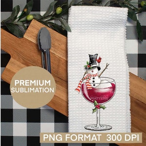 May include: A white kitchen towel with a snowman in a red wine glass. The snowman is wearing a black top hat with white polka dots, a red and white striped scarf, and a red cardinal perched on his hat. The glass is filled with red wine and has a green holly sprig on the stem. The towel is on a black and white checkered background.