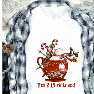 K&ouml;nnte beinhalten: Ein wei&szlig;es T-Shirt mit einem roten Becher-Design, das einen Schneemann, Zuckerstangen und den Text "Fueled by Tea & Christmas!" zeigt.