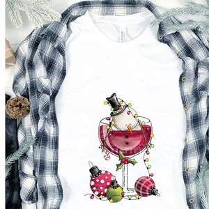 May include: A white snowman wearing a black top hat is submerged in a glass of red wine. The snowman is decorated with a string of white lights. Three Christmas ornaments are scattered around the base of the glass.