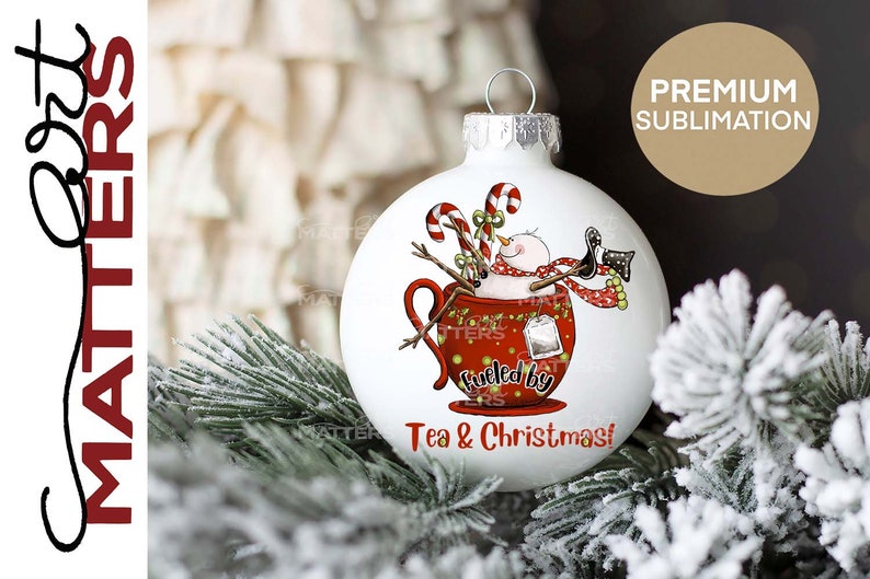 K&ouml;nnte beinhalten: Wei&szlig;er Weihnachtsbaumschmuck mit einem Schneemann in einer roten Teetasse. Der Schneemann tr&auml;gt einen roten Schal und h&auml;lt einen Zuckerstock. Der Text auf dem Ornament lautet "Fueled by Tea & Christmas!"