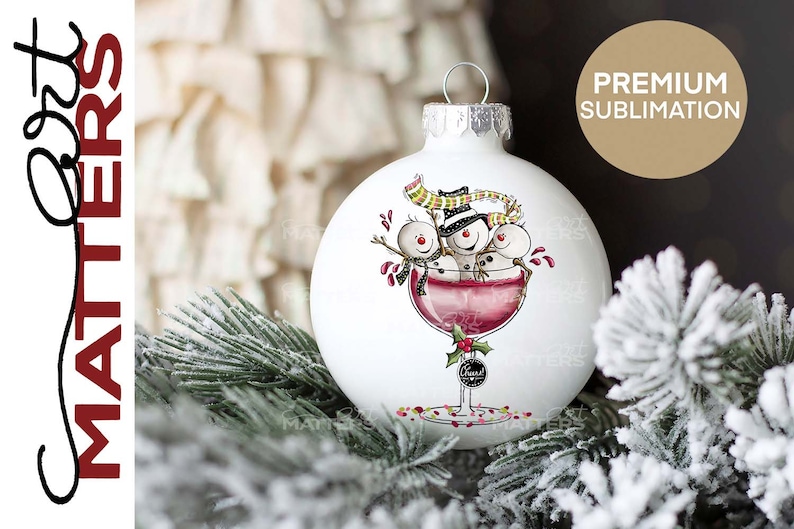 May include: White Christmas ornament with three snowmen in a wine glass. The snowmen are wearing hats and scarves. The wine glass is filled with red wine and has a holly sprig on the stem. The ornament is surrounded by a snowy pine branch.