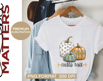 May include: A white t-shirt with a design of three pumpkins. The pumpkins are decorated with different patterns. The text "Hello Fall" is written below the pumpkins.