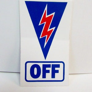 May include: A white sticker with a blue triangle containing a red lightning bolt. The word "OFF" is written in blue letters on a white rectangle.