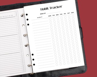 May include: A black leather bound planner with a white page open to a habit tracker. The tracker has a section for the week of, a habit list, and columns for each day of the week: Monday, Tuesday, Wednesday, Thursday, Friday, Saturday, and Sunday. Each day has a row of circles for tracking habits.