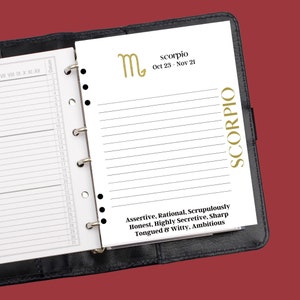 May include: A black leather bound planner with a white page open to the Scorpio zodiac sign. The page features the Scorpio symbol, dates, and a description of the Scorpio personality traits: Assertive, Rational, Scrupulously Honest, Highly Secretive, Sharp Tongued & Witty, Ambitious.