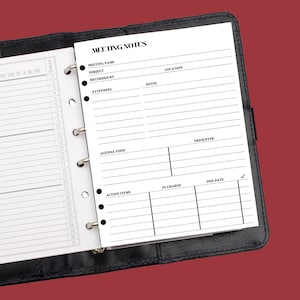 May include: Open black leather binder with a white paper insert labeled "MEETING NOTES." The insert has sections for meeting details, attendees, agenda, and action items. A calendar is visible on the left side.
