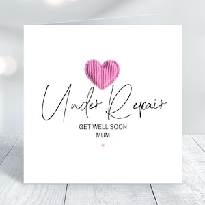 May include: A white card with a pink heart and the text "Under Repair" in black script. Below the text is "Get Well Soon Mum" in smaller black text.