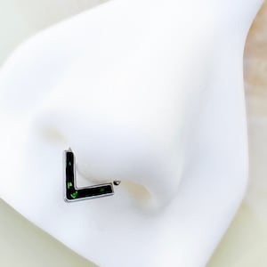 May include: A black L-shaped nose ring with green glitter embedded in the metal.