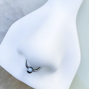 May include: A silver nose ring with a clear opal gemstone. The ring is on a white mannequin.