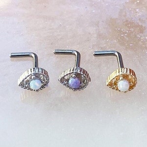 May include: Three silver nose rings with a decorative eye design and a small opal gemstone in the center. The opal gemstones are white, purple, and light blue.