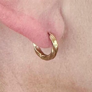 May include: A close-up of a person's ear with a gold hoop earring. The earring is textured and has a hammered finish.