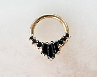 May include: Gold hoop earring with a row of black baguette-shaped stones set in a crescent shape.
