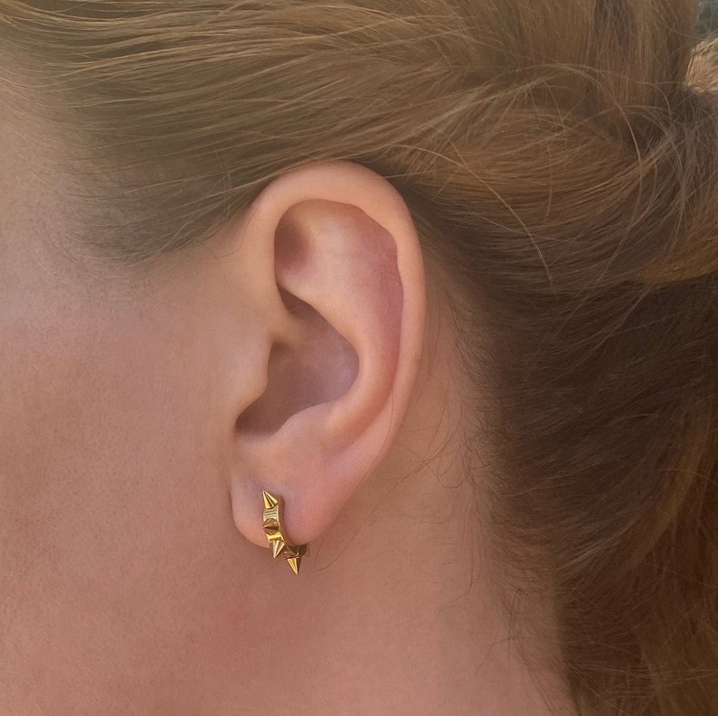 May include: Gold hoop earrings with small, pointed spikes around the edge.