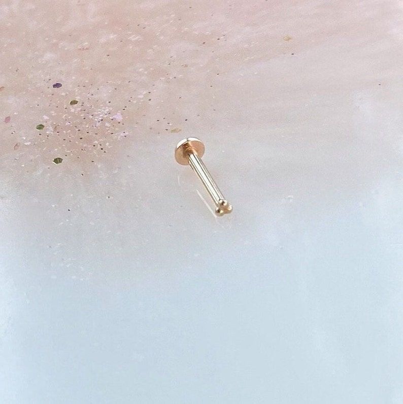 May include: A gold nose ring with a small ball on one end and a three-ball cluster on the other end.