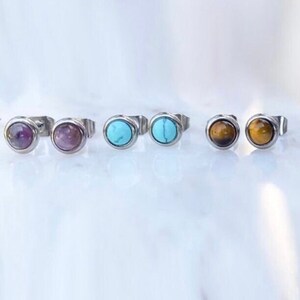 May include: Six pairs of small, round stud earrings with different colored stones. The earrings are made of silver and have a simple design. The stones are amethyst, turquoise, and tiger's eye.