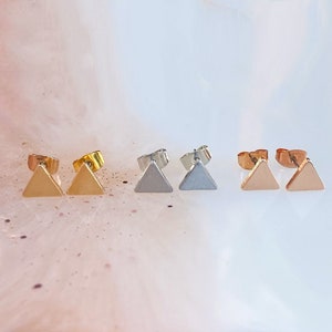 May include: Three pairs of triangle-shaped earrings in gold, silver, and rose gold.