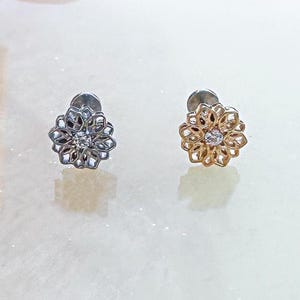 May include: Two flower-shaped earrings with a clear gemstone in the centre. The earring on the left is silver and the earring on the right is gold.