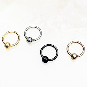 May include: Four different colored circular hoop earrings with a ball at the end. The hoops are silver, gold, black, and rose gold.