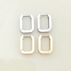 May include: Four pairs of rectangular hoop earrings. Two pairs are silver-colored, and two pairs are gold-colored. Each earring has a hinged closure with a straight bar. The earrings are displayed on a light beige surface.