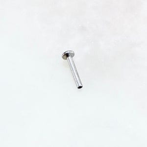 May include: A small, silver-colored flat back stud earring. The earring has a flat, round top and a straight post. The earring is shown on a white background.