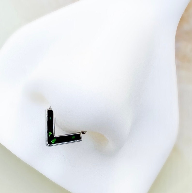 May include: A black L-shaped nose ring with green glitter embedded in the metal.