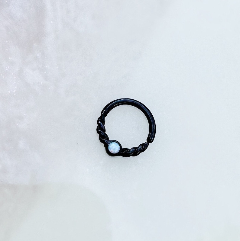 May include: Black twisted ring with a white opal gemstone.