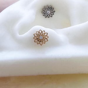 May include: A gold flower-shaped body jewellery piece with a clear gemstone in the centre.