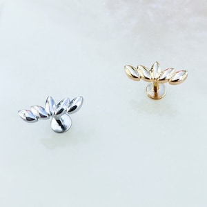 May include: Two silver and gold leaf-shaped body jewelry pieces with a post and ball closure. The jewelry is on a white background.