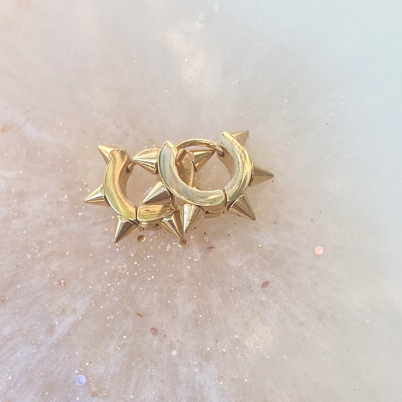 May include: A pair of gold hoop earrings with sharp, pointed spikes around the edges.