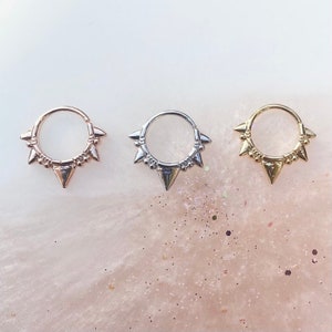 May include: Three gold, silver, and rose gold hoop earrings with a row of small spikes around the hoop.