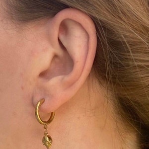 May include: Gold hoop earrings with a small gold skull charm dangling from the bottom.