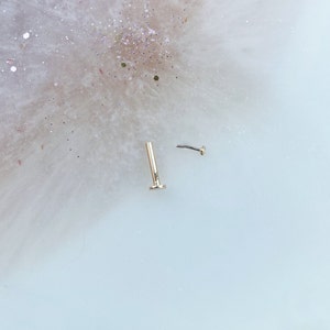 May include: Two gold nose rings, one with a flat top and one with a curved top.