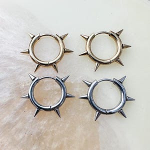 May include: Four hoop earrings with a starburst design. Two earrings are gold and two are silver. Each earring has a circle with eight points.
