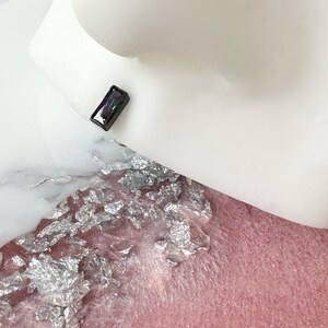 May include: A small, iridescent, rectangular-shaped gemstone with a black base and a rainbow sheen.