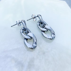 May include: A pair of silver-colored chain link earrings. Each earring features two elongated oval links connected by a twisted link. The earrings have a post and butterfly backing. The jewelry is displayed on a white surface.