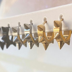 May include: A set of five hoop earrings with a row of spikes around the hoop. The earrings are available in black, silver, and gold.