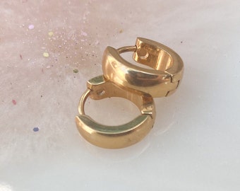 Puede incluir: Un par de pendientes de aro de oro. Los pendientes están hechos de un metal grueso y liso y tienen un diseño simple y clásico.