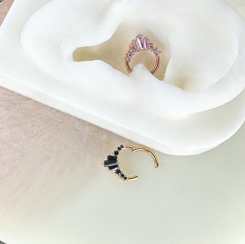 Pode incluir: Dois brincos de argola de ouro com uma fileira de pequenas pedras de zirc&ocirc;nia c&uacute;bica transparentes. A argola da esquerda tem pedras pretas e a argola da direita tem pedras rosa.
