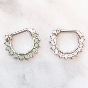 Puede incluir: Dos anillos de septum plateados con una fila de gemas transparentes y de color ópalo alrededor del anillo.