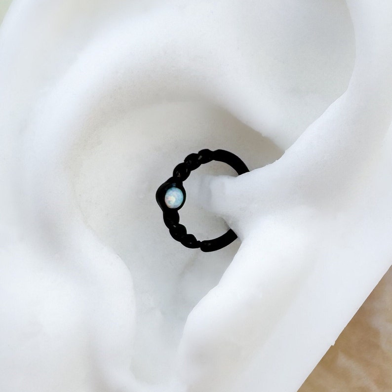 May include: Black hoop earring with a small opal gemstone. The earring is shown in a white background.